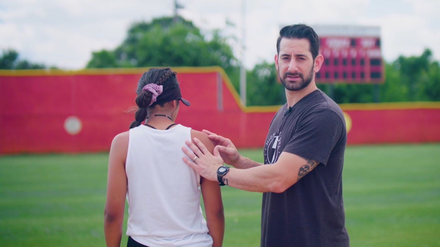Coach demonstrating shoulder blade movement on a softball athlete
