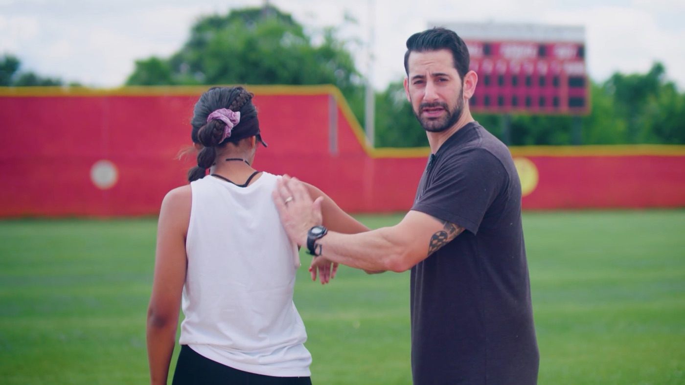 Coach demonstrating scapular movement with a softball athlete on the field